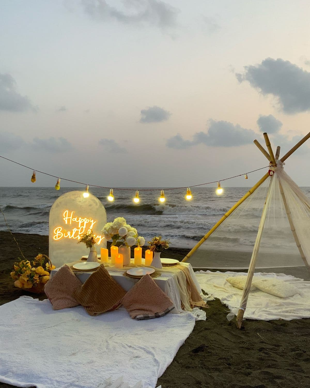 A private beachside dinner setup with string lights and a Happy Birthday sign